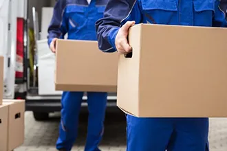 Mover carrying a cardboard box in a home relocation setting.