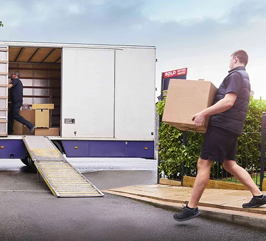 A mover pushing a dolly with a large item onto a truck ramp, illustrating long-distance moving solutions.