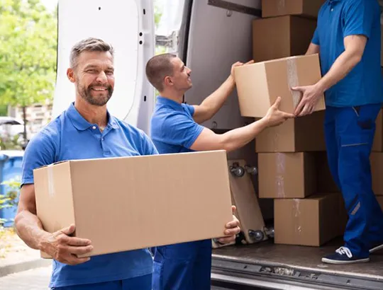 Smiling movers in blue uniforms carrying cardboard boxes.