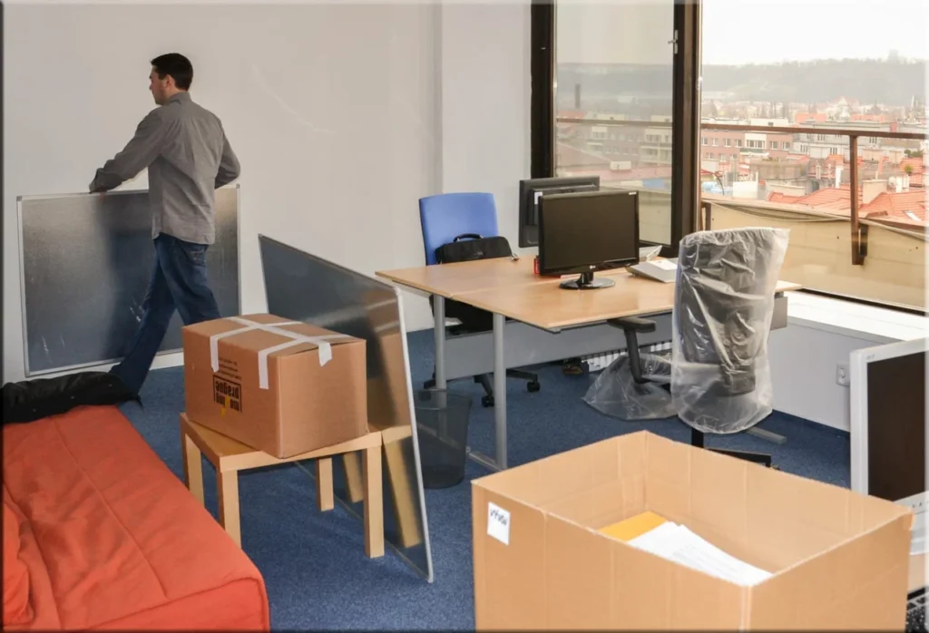 An office space being packed for moving, with a man handling a panel and cardboard boxes scattered around in Edmond, OK.